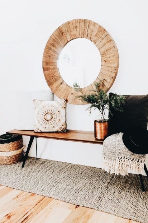 a boho chic space with a printed folksy rug, a wooden bench, an embroidered pillow, a basket, a blanket and a wood clad mirror