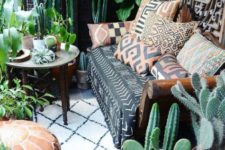 a boho desert porch with cacti, greenery, statement plants, a sofa with printed pillows and a carved wooden table