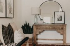 a boho entryway with a vintage inlay console table, a woven bench and matching contrasting pillows, artworks and a large rug