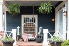 a boho porch with a large rattan loveseat, pillows, an ottoman, potted greenery and lanterns