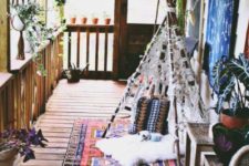 a boho porch with potted greenery hung here and there, a macrame teepee, a boho rug and lanterns