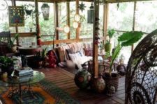 a boho screened porch, rattan and wooden furniture, lanterns, potted greenery, boho textiles and artworks