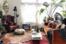 a boho space with a rust velvet sofa, boho rugs and ottomans, floor lamps and potted plants