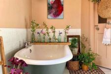 a bold boho meets vintage bathroom with buttermilk walls, a bold rug, a grey clawfoot tub, potted greenery and wicker touches