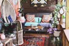 a bright boho porch with a wicker sofa and a peacock chair, a hairpin leg table, a geometric artwork, lights, boho textiles and lots of decor