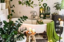 a calming boho bathroom with potted plants, green touches, a free-standing bathtub, candles and a rug on the floor