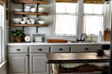 a chic farmhouse kitchen with vintage grey cabinets, floating wooden shelves, a shabby chic stained table as a kitchen island