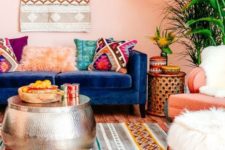 a colorful boho living room with bright lampshades, pink walls, boho rugs and pillows and a hammered metal coffee table