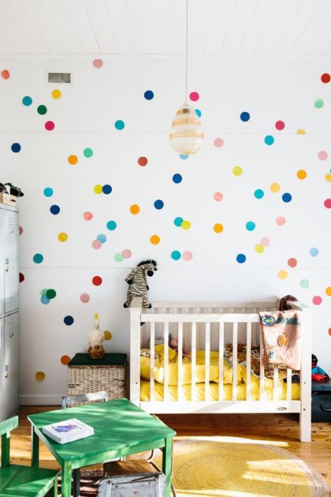 a colorful gender neutral nursery with colorful polka dots, bright bedding and green furniture