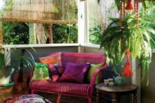 a colorful screened gypsy porch with potted greenery, a hot pink loveseat, a carved wooden table and colorful pillows