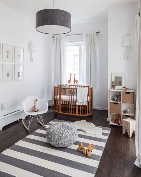 a contemporary nursery with a striped rug, a grey lamp and ottoman, a gallery wall and a cool stained crib