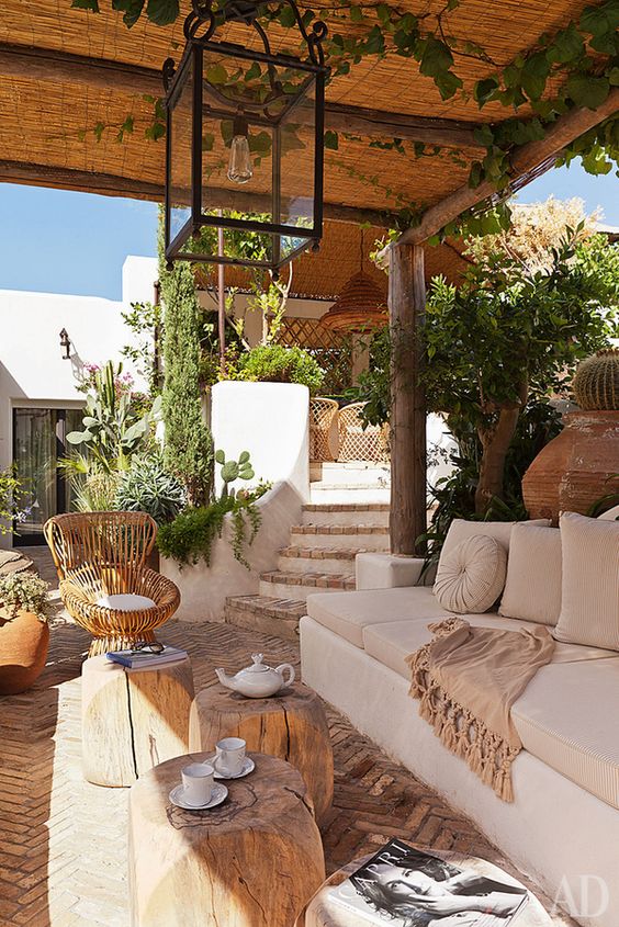 a contemporary rustic terrace with neutral furniture, a glass lamp, wooden stools and a rattan chair