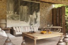 a country patio with rustic wicker furniture, a vintage wooden table, oversized candle lanterns and a statement artwork