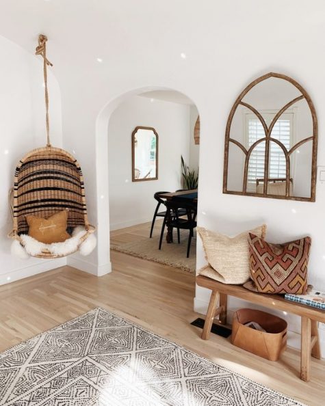 a cozy boho entry with a wooden bench, a leather bag for storage, boho pillows, a framed window like mirror, a boho rug and a wicker hanging chair