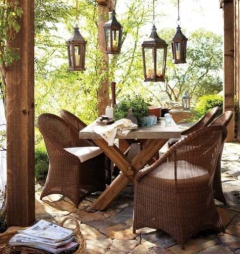 a cozy rustic patio with wicker chairs, a wooden table and wooden lanterns hanging over the table