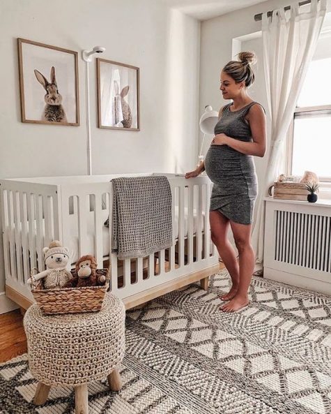 a gender neutral nursery with bunny artworks, a woven rug and ottoman on wooden legs