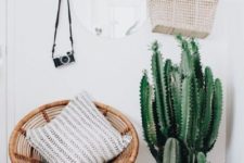 a gorgeous boho entryway with potted cacti, a suspended mirror on leather loops, a wicker chair and a vintage camera