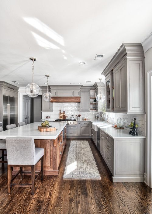 a grey farmhouse kitchen with a large stained kitchen island, a white tile backsplash and vintage cabinets