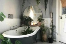 a hippie bathroom with a greye clawfoot tub, a printed rug, a large mirror and lots of potted plants here and there