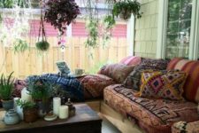 a large boho porch with an L-shaped sofa with boho upholstery, a dark stained chest, a leather ottoman and suspended planters