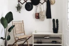 a monochromatic boho entryway with a white shoe shelf, a printed rug, a black rack, a woven chair and potted plants