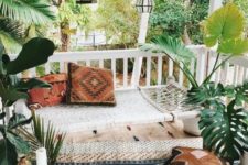 a relaxed and neutral boho porch with a daybed, boho pillows and a rug, candle lanterns, potted plants and a plywood box