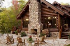 a rustic patio with a large fireplace clad with stones, simple wooden chairs and potted blooms and greenery