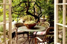 a rustic patio with rattan chairs, an elegant vintage table and potted plants all around