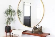 a simple boho entry with a boho rug, a rich stained wooden bench, an oversized round mirror, a black planter on a stand