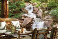 a simple rustic patio with wooden upholstered furniture, a cool coffee table and a fantastic waterfall right next to the space