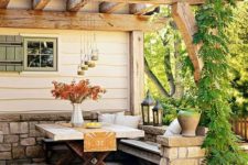 a small and cozy rustic patio with a built-in bench, a wooden trestle table and some hanging and usual lanterns