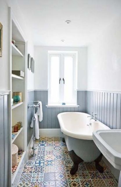 a small and narrow bathroom with light blue wainscoting on the walls and colorful printed tiles on the floor