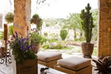 a small rustic patio with wicker poufs and chairs, a reclaimed wooden table and lots of blooms and cacti in pots
