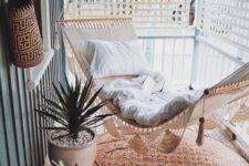 a small screened porch with a woven and macrame hammock, potted succulents and a boho printed rug