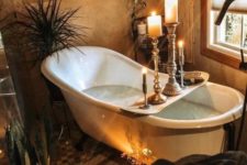 a spiritual bathroo with decorative baskets on the wall, candles, potted plants and greenery and a vintage bathtub