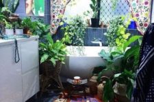 a super colorful boho bathroom with a bright curtain, lots of potted greenery around, a boho rug, an artwork and candles