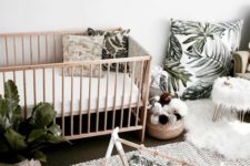 a tropical nursery done in neutrals, with tropical leaf prints and much potted greenery, a jute rug and a wooden crib