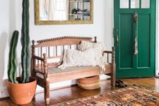 a vintage boho entryway with a vintage carved wooden bench, a boho rug, a potted cactus, a mirror in a gold ornate frame