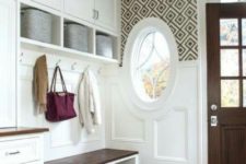 a vintage farmhouse entryway with white wainscoting on the walls and a round window that matches