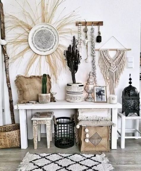 a whimsical whitewashed boho entryway with macrame hangings, potted cacti, a decorative plate with grass, a console and some catchy stools and a boho rug