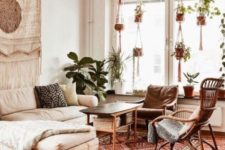 an elegant boho living room with rattan and wood furniture, boho rugs and pillows, planters in macrame hangers and a macrame hanging on the wall