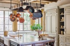 an elegant vintage farmhouse kitchen with neutral cabinets going up to the ceiling, a hanger for pans and a large kitchen island