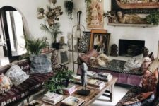 an epic gypsy living room with dark embroidered furniture, pendant lamps, a fireplace and boho pillows and artworks