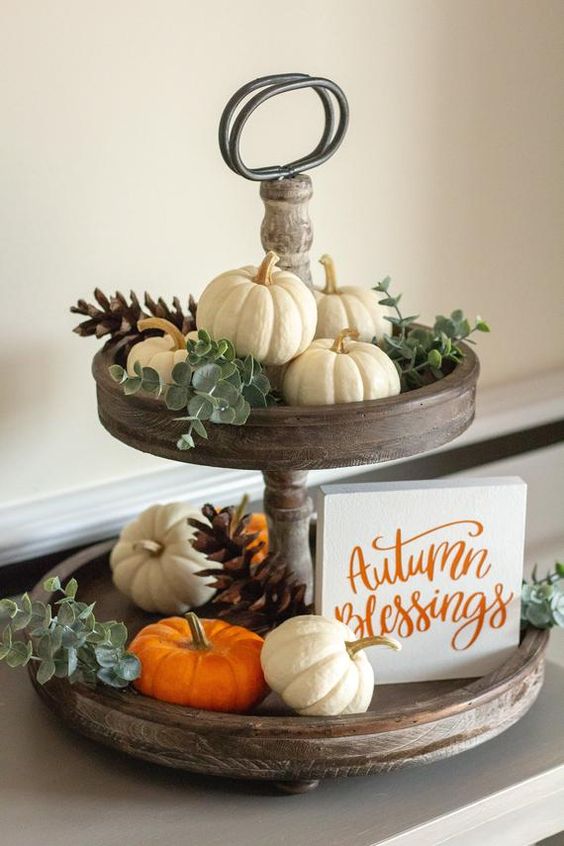 a wooden stand with eucalyptus, white and orange pumpkins and pinecones and a small sign