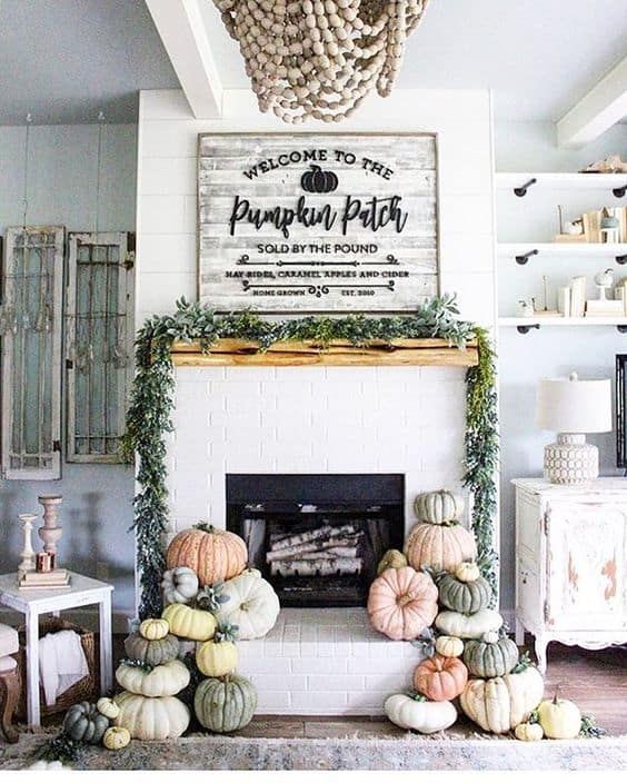 a fall fireplace display with lots of heirloom pumpkins, a greenery garland on the mantel and a sign