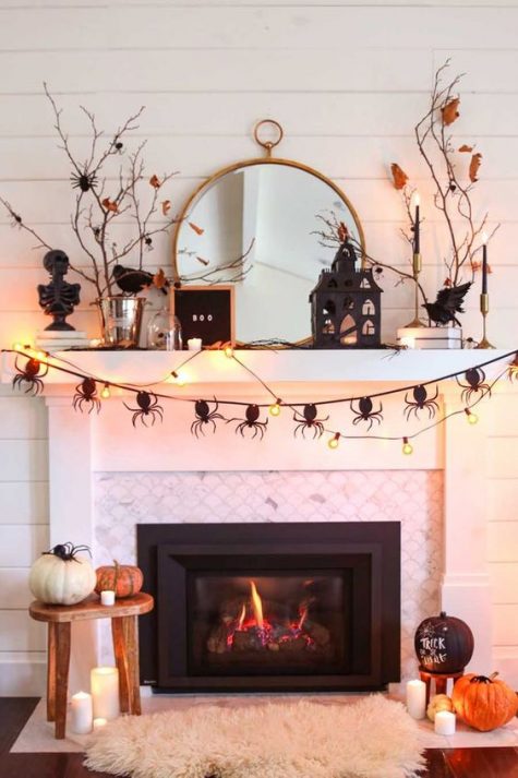 a Halloween mantel and fireplace with a spider bunting, lights, pumpkins, lanterns and candles
