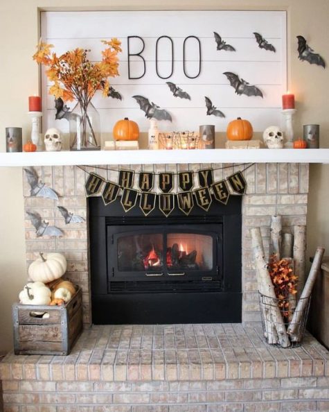 a Halloween mantel with pumpkins, bats, fall leaves, candles and a crate with natural pumpkins