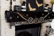 a black and gold mantel with bats, a bunting, candles, striped jars with branches, painted pumpkins and a pillow