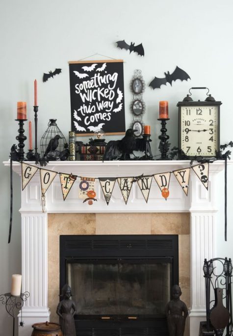a bold Halloween mantel with bats, a bunting, a cage with a blackbird, candles, a clock and a sign