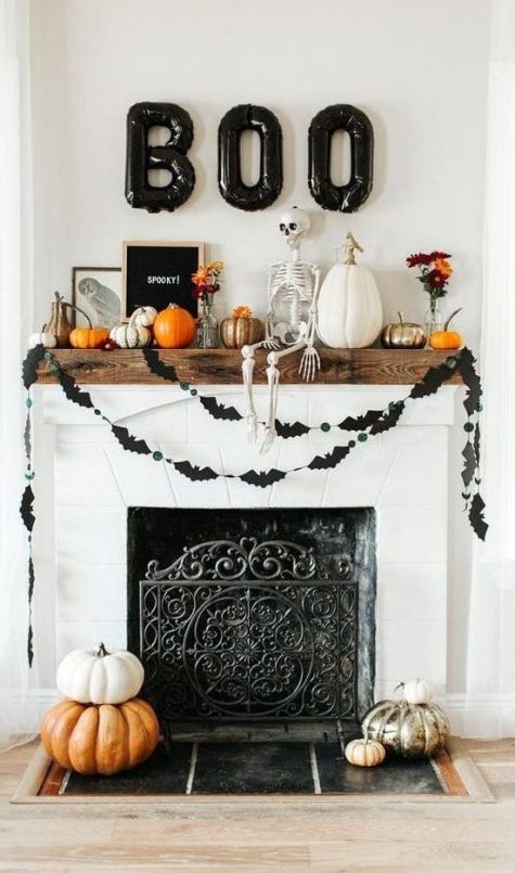 a bright Halloween mantel with a bat bunting, natural and painted pumpkins, a skeleton, black balloon letters and a sign